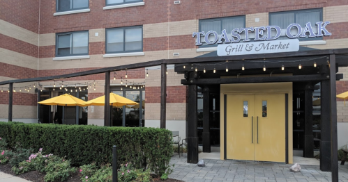Exterior of Toasted Oak Grill & Market, featuring yellow umbrellas, string lights, and a welcoming entrance.