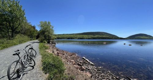 Two bicycles parked by a serene lake, surrounded by lush greenery and mountains under a clear blue sky.