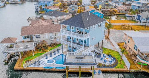 Aerial view of a colorful waterfront house with a pool, surrounded by other homes and water.