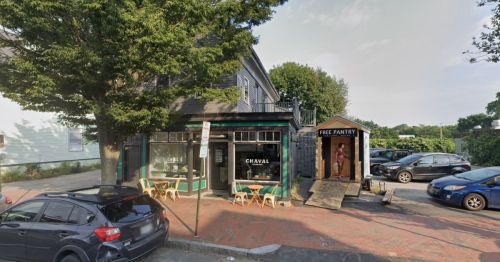 A small restaurant with outdoor seating next to a free pantry structure on a tree-lined street.