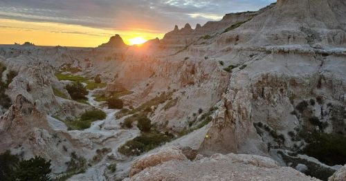 Sunset over rugged Badlands terrain, highlighting unique rock formations and a serene valley.