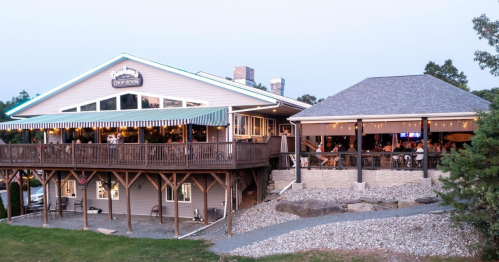 A cozy restaurant with outdoor seating, surrounded by trees and gravel, bustling with diners during sunset.