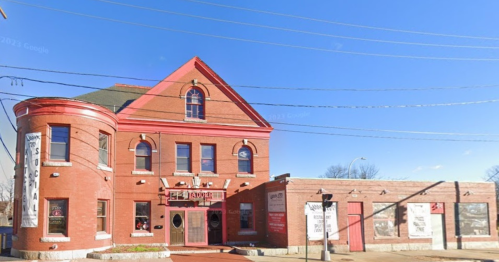 Historic red brick building with large windows and a distinctive curved entrance, set against a clear blue sky.
