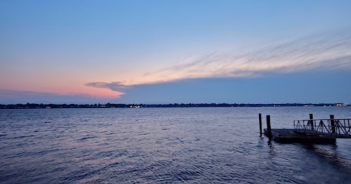 A serene waterfront scene at dusk, featuring calm water and a colorful sky with soft clouds.