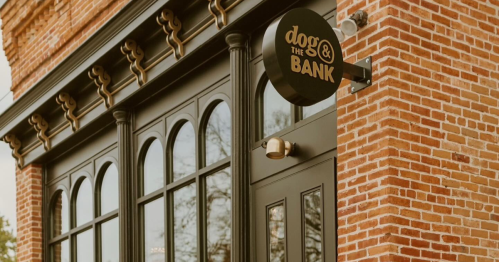 Exterior of a brick building featuring a sign that reads "dogs & the BANK" with large arched windows.