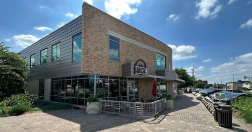 A modern café building with large windows, a sign reading "Cafe," and outdoor seating on a sunny day.