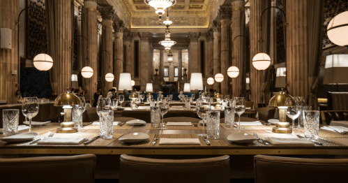 Elegant restaurant interior with a long table set for dining, featuring crystal glassware and stylish lighting.