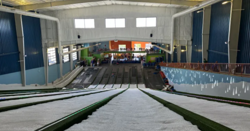 View from the top of a snow tubing slope inside an indoor facility, with people in the background.