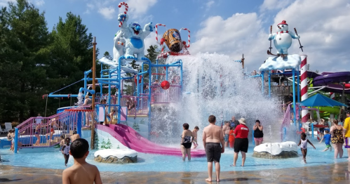 A water park scene with colorful slides, a splash pad, and people enjoying the water on a sunny day.