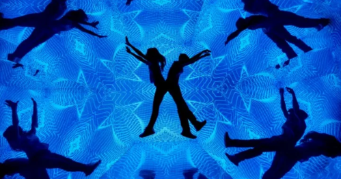 Silhouettes of dancers against a vibrant blue kaleidoscopic background, creating a dynamic and energetic scene.