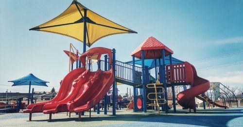 Colorful playground with red slides, blue structures, and yellow canopies under a clear blue sky.