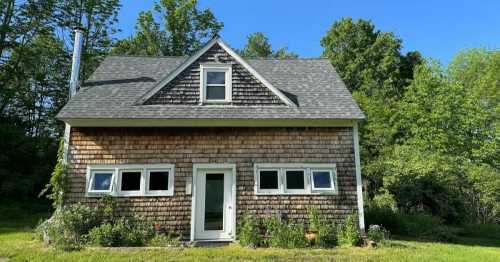 A charming wooden cottage with a sloped roof, surrounded by greenery and blue skies.