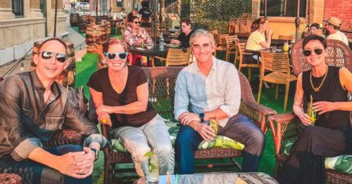 A group of four people sitting outdoors at a social gathering, enjoying drinks and smiling at the camera.