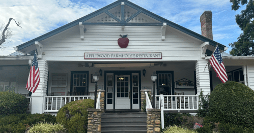 Exterior of Applewood Farmhouse Restaurant, featuring a white facade, American flags, and a prominent apple sign.