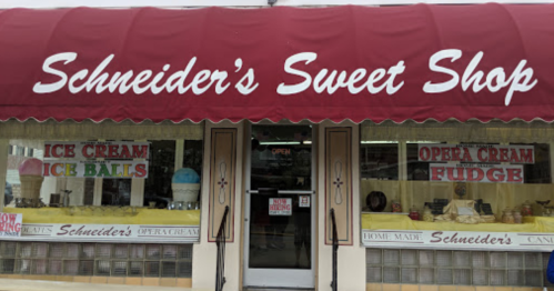 A storefront with a red awning reading "Schneider's Sweet Shop," featuring signs for ice cream and fudge.