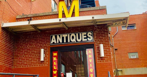 A brick building with a large "M" sign above a door labeled "ANTIQUES" in bright letters.