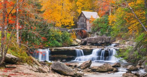 A scenic view of a wooden mill by a waterfall, surrounded by vibrant autumn foliage.