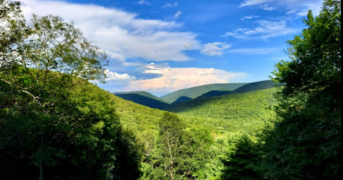 A panoramic view of lush green mountains under a bright blue sky with scattered clouds.