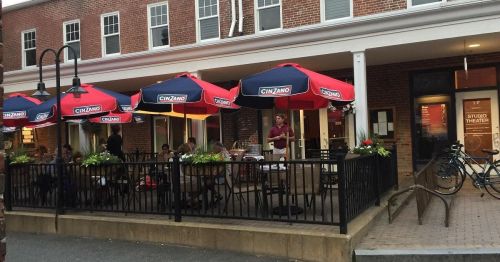 Outdoor dining area with red umbrellas, people seated, and a nearby bike rack in front of a theater.