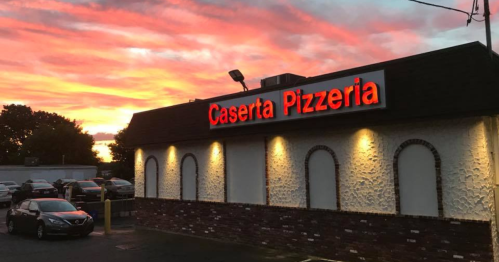 A pizzeria building with a bright sign against a colorful sunset sky.