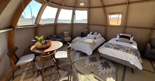 Cozy interior of a glamping tent featuring two beds, a dining table, and comfortable seating with natural light.