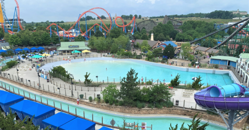 Aerial view of a water park featuring a wave pool, lazy river, and roller coasters in the background.