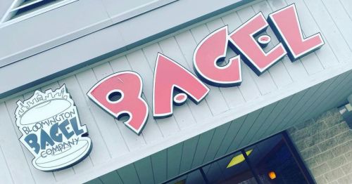 Sign for Bloomington Bagel Company featuring the word "BAGEL" in bold red letters on a light-colored building.