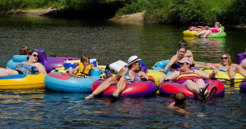 A group of people relax on colorful inner tubes in a river, enjoying a sunny day.