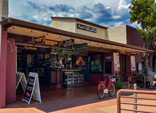 A colorful storefront featuring a gelato shop with outdoor seating and a bicycle parked nearby under a cloudy sky.