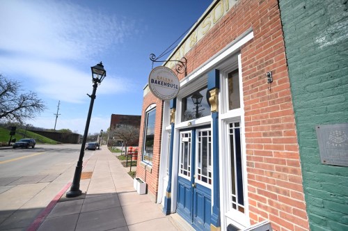 A brick building with a blue door and a sign reading "Bakerhouse" on a sunny street.