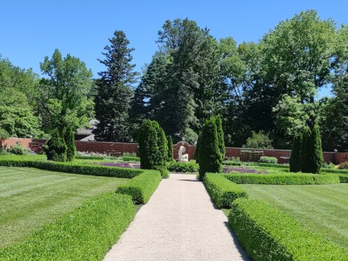 A well-maintained garden with neatly trimmed hedges, a gravel path, and lush greenery under a clear blue sky.