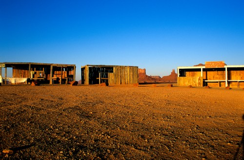 Desert landscape with wooden structures and a clear blue sky, evoking a rustic, abandoned atmosphere.