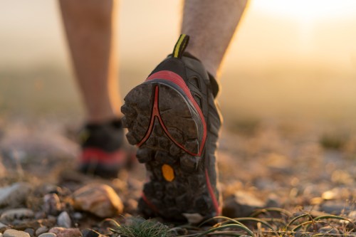 Close-up of a person's shoe walking on rocky terrain during sunset, highlighting the shoe's tread and details.