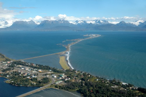 Aerial view of a coastal landscape with mountains, a winding road, and a peninsula extending into the ocean.