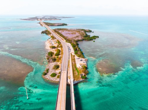 Aerial view of a long bridge extending over turquoise waters, connecting to a small island with lush greenery.
