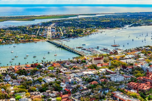 Aerial view of a coastal town with a marina, bridges, and lush greenery along the water's edge.