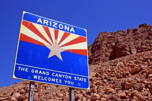 Sign welcoming visitors to Arizona, featuring the state flag design and text: "The Grand Canyon State Welcomes You."