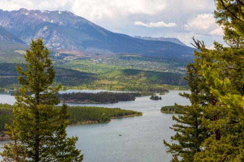 A scenic view of a lake surrounded by lush greenery and mountains under a partly cloudy sky.