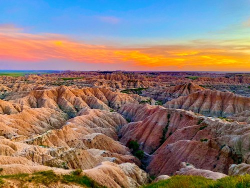 A stunning sunset over the rugged, colorful Badlands landscape, showcasing layered hills and valleys.