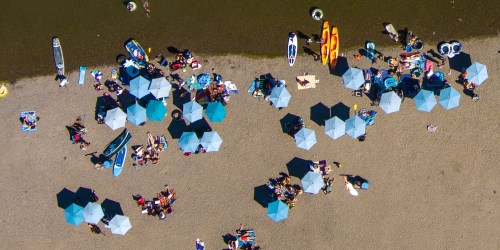 Aerial view of a beach with umbrellas, people sunbathing, and various watercraft along the shore.