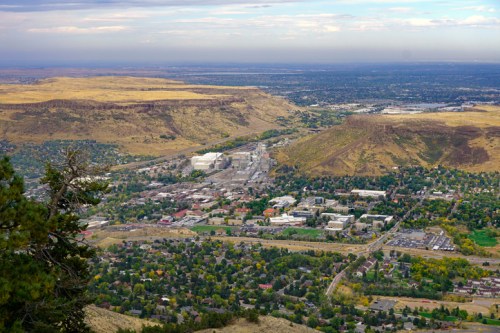 Aerial view of a valley with a town, surrounded by hills and open land under a cloudy sky.