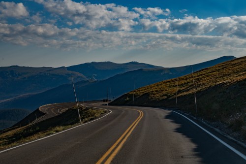 Winding road through mountainous terrain under a blue sky with scattered clouds.