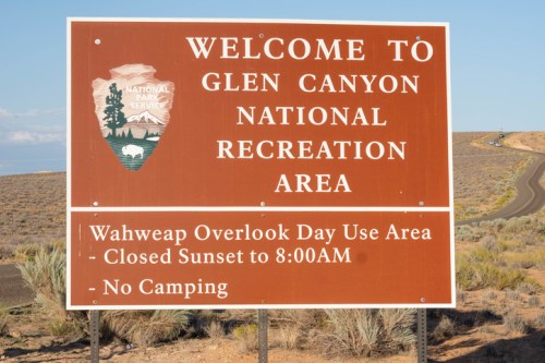 Sign welcoming visitors to Glen Canyon National Recreation Area, noting Wahweap Overlook hours and no camping policy.