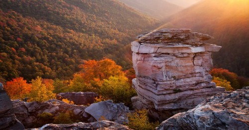 A towering rock formation amidst vibrant autumn foliage and rolling hills, illuminated by warm sunlight.