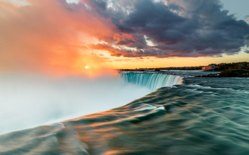 A stunning sunset over Niagara Falls, with vibrant colors reflecting on the water and mist rising from the falls.
