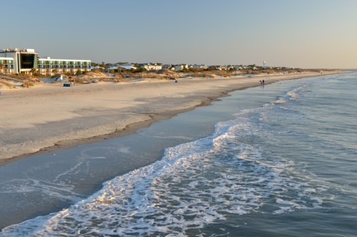 A serene beach at sunset, with gentle waves lapping the shore and a distant hotel along the coastline.