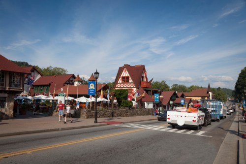 A charming street scene featuring German-style buildings, outdoor dining, and vehicles on a sunny day.