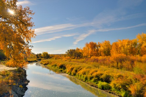 A serene river flows through a landscape of vibrant autumn foliage under a clear blue sky.