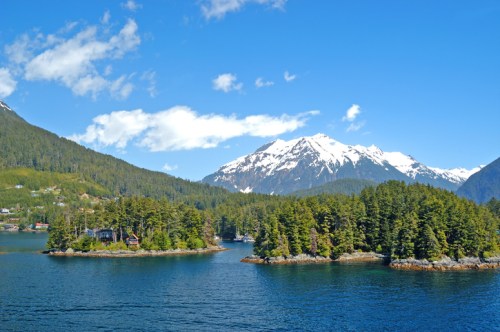 Scenic view of snow-capped mountains and lush green islands reflecting in calm blue waters under a clear sky.