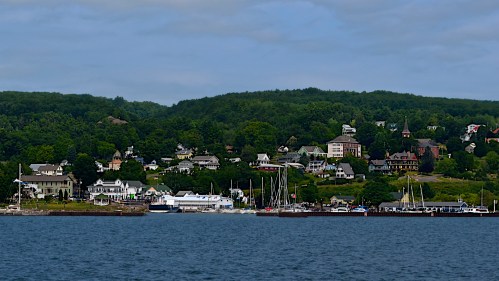 A scenic view of a waterfront village with lush green hills, boats docked, and charming houses along the shore.
